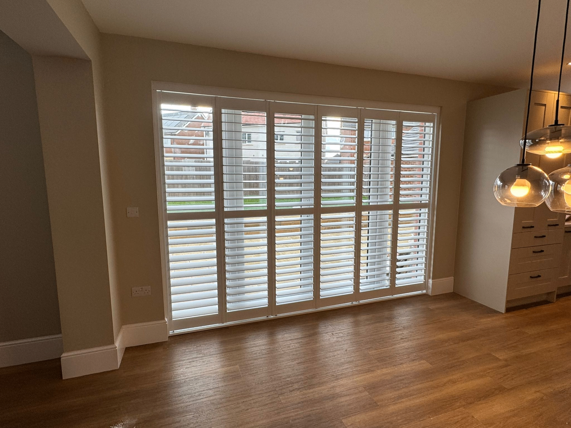 Six-panel white tracked bifold shutters closed across a wide dining room window
