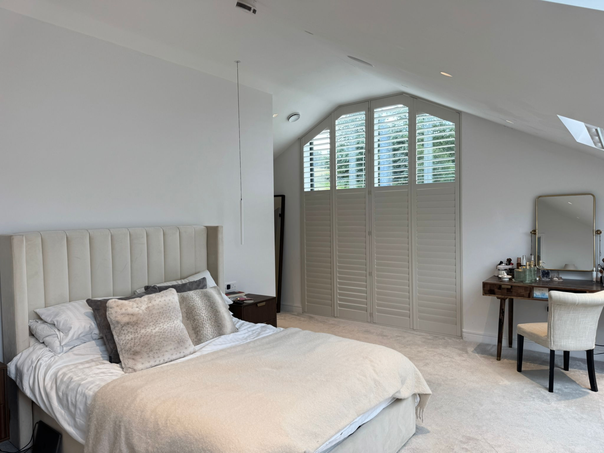 Bedroom with shaped shutters partially closed across a tall angled gable window
